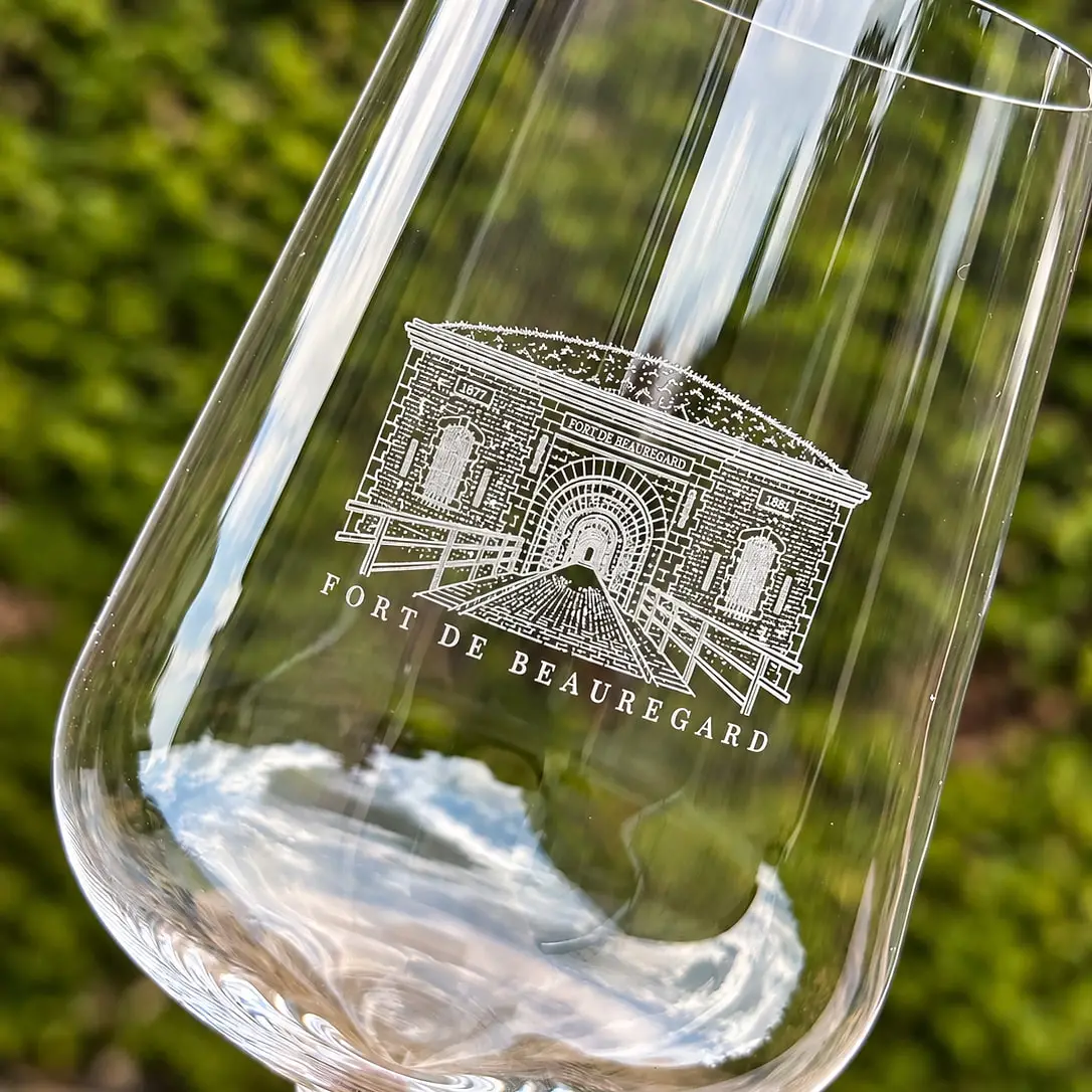 Verre à dégustation Glassora gravé du blason du Fort de Beauregard, tenu devant une haie