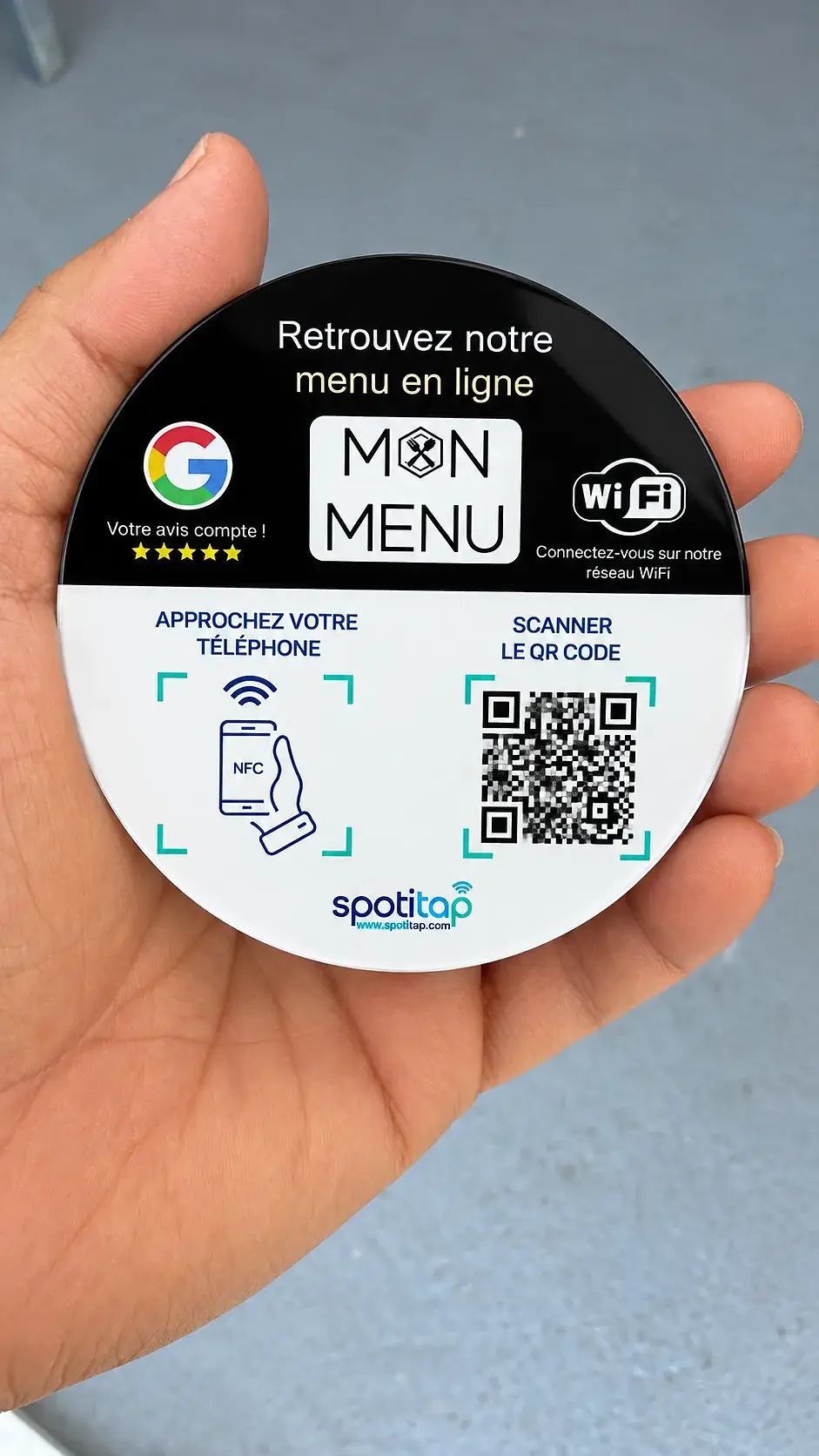 Plaque ronde NFC réunissant menu en ligne, avis Google et accès Wi-Fi, tenue dans une main